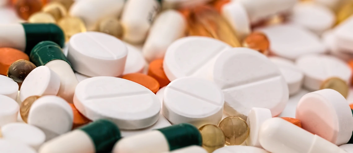 Close-up of assorted pills and capsules, including white tablets, orange tablets, and green-and-white capsules scattered together.