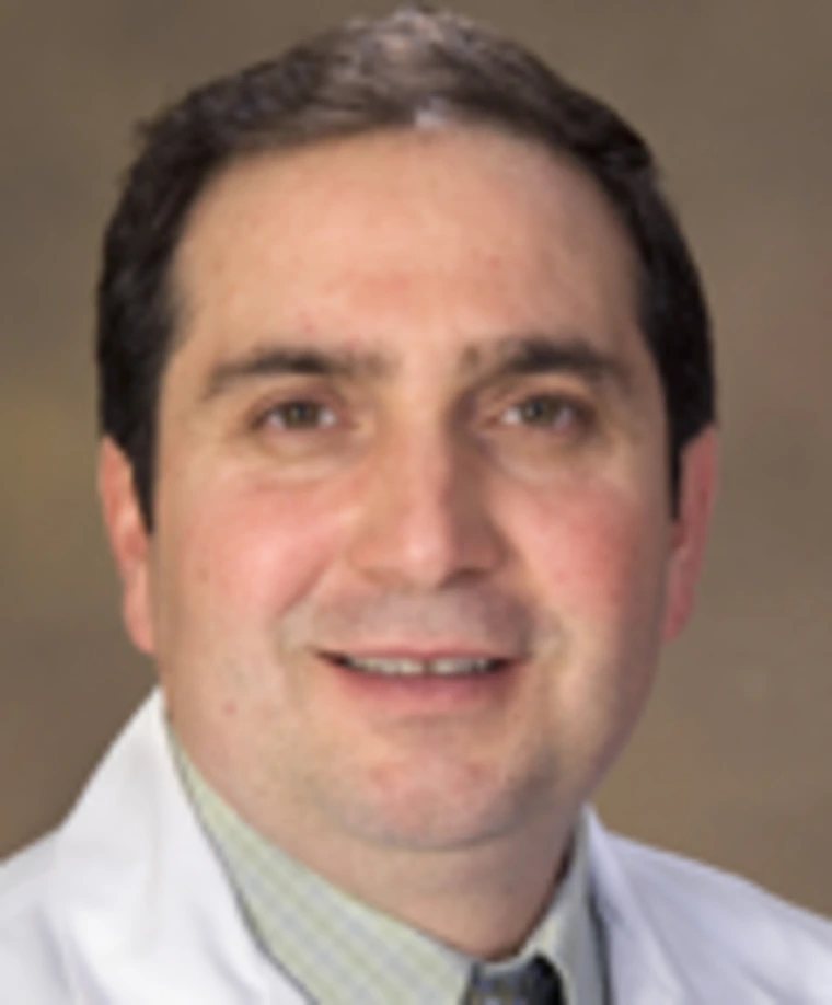 Person wearing a white lab coat and light green shirt smiling at the camera.