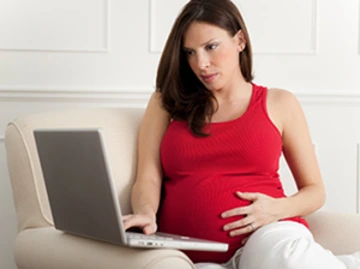 Pregnant woman sitting on a couch using a laptop.