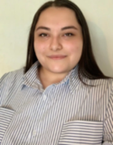 Person with long straight hair wearing a striped button-up shirt smiling in front of a light background.